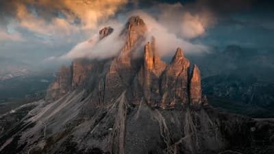 Majestic peaks pierce through the mist, glowing warmly as golden light embraces the rugged stone giants of the wild. 🏔️