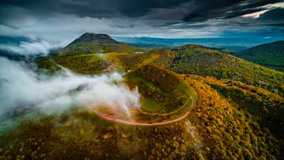 Mystical clouds drift over vibrant autumn hills, where a winding road leads into the heart of an enchanting, moody landscape. 🍁
